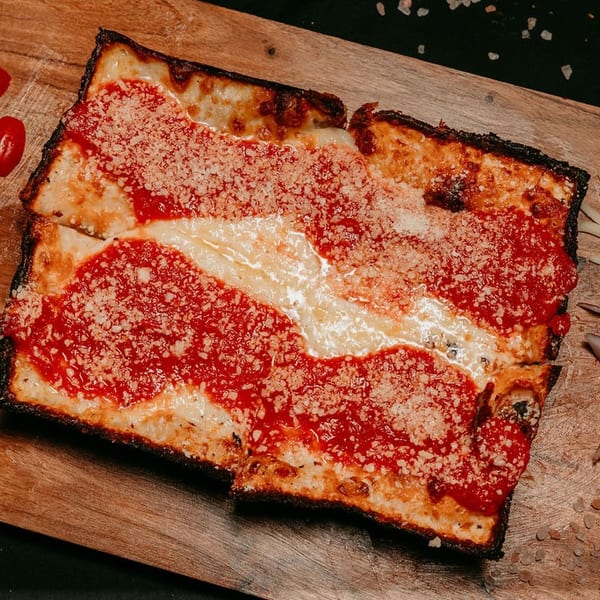 Detroit-style pizza with red sauce, melted cheese, and parmesan on a wooden board.