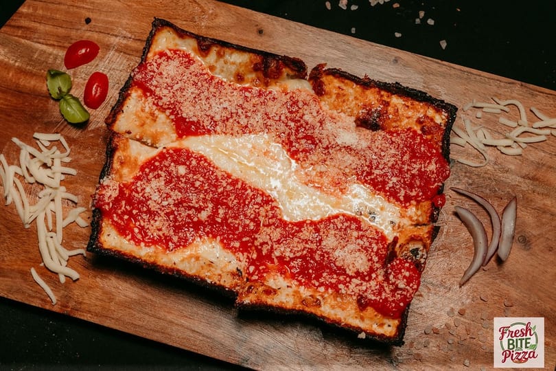 Detroit-style pizza with red sauce, melted cheese, and parmesan on a wooden board.