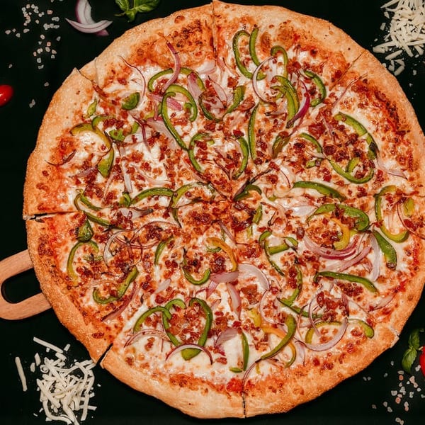A Fresh Bite Pizza with green peppers, red onions, and bacon bits on a dark surface.