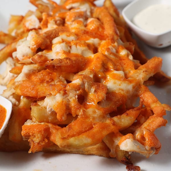 A plate of cheesy fries topped with orange sauce and white cheese, with two dipping sauces.