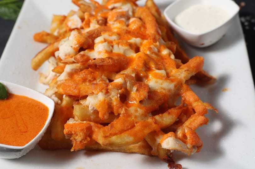A plate of cheesy fries topped with orange sauce and white cheese, with two dipping sauces.