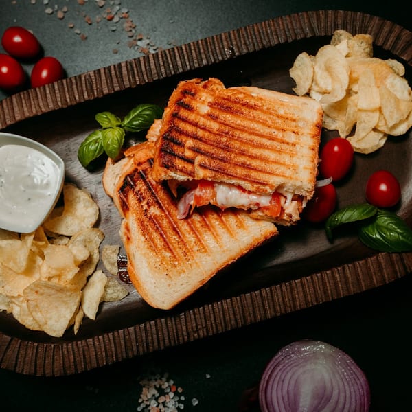 Grilled panini sandwich with melted cheese, tomatoes, and onions, served with chips and dip.