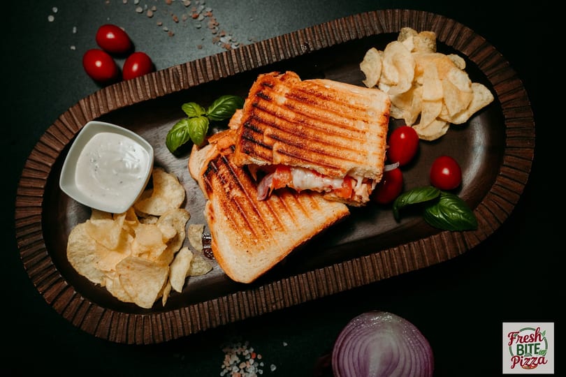 Grilled panini sandwich with melted cheese, tomatoes, and onions, served with chips and dip.