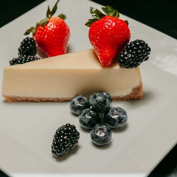 Slice of cheesecake with strawberries, blueberries, and blackberries on a white plate.