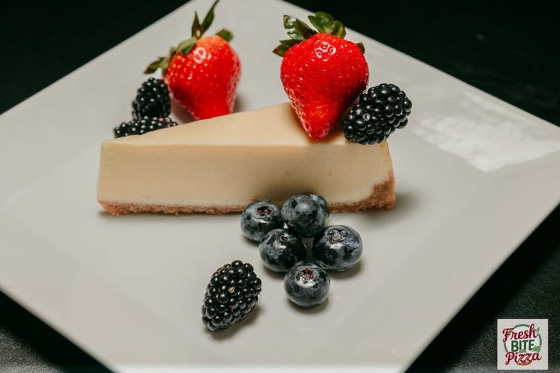 Slice of cheesecake with strawberries, blueberries, and blackberries on a white plate.